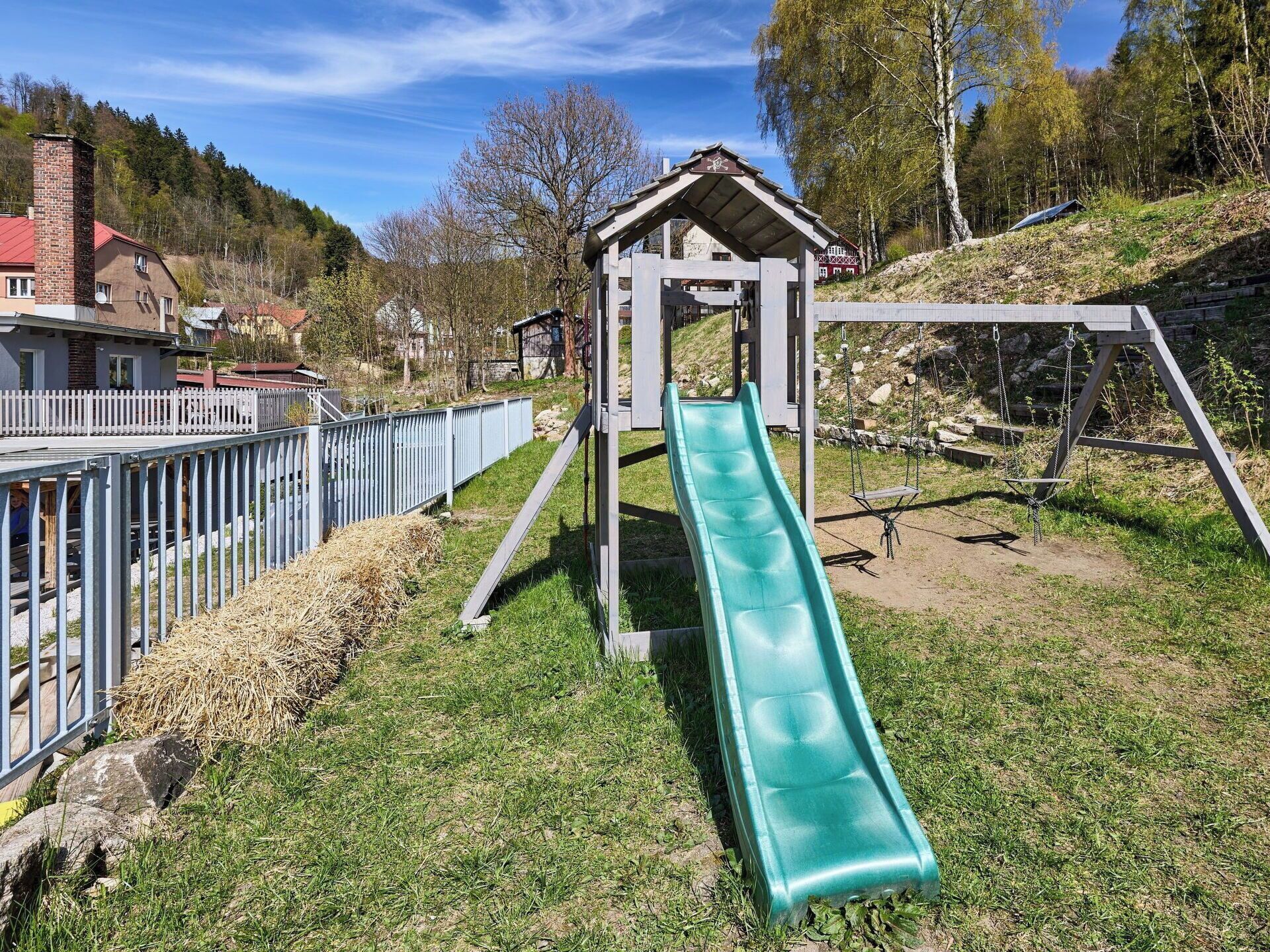 Une aire de jeux avec un toboggan, des balançoires et un petit abri.