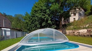 Ein Schwimmbecken mit einer klaren Abdeckung, umgeben von einer Betonplattform und einem Metallzaun.