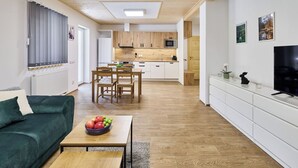 Ein modernes Wohnzimmer mit einer Couch, einem Esstisch und einer Küchenzeile mit Holdekor und einem Fernseher.
