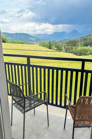 Ein Balkon mit zwei Korbstühlen, Blick auf ein grünes Feld und ferne Berge.