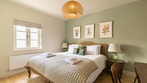 A bedroom with a bed, bedside lamps, a window with blinds, and framed botanical prints on the wall. - Your Place - 2 bedroom Mews House in Notting Hill (London)