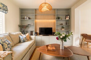 Ein modernes Wohnzimmer mit Sofa, Couchtisch, Fernseher und Regalen mit Dekoration.