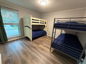 Ein Zimmer mit zwei Etagenbetten, einem aus Holz und einem aus Metall, einem Fenster mit Jalousien und einem Holzboden.