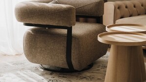 En moderne stue med en polstret sofa, et rundt træbord og en armstol med struktur.