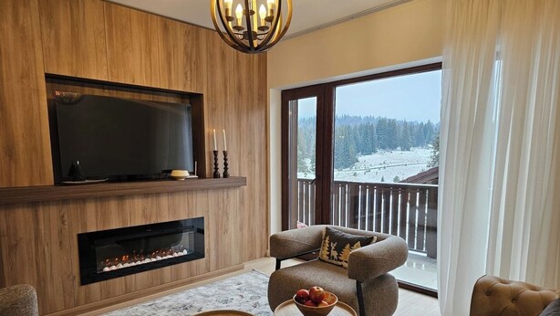 En moderne stue med pejs, fjernsyn og en balkon med udsigt over et sneklædt landskab.