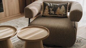 En hyggelig lænestol med pude med skovmotiv, placeret på et mønstret tæppe.