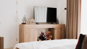 Et moderne soveværelse med en seng, et fjernsyn på et træskab, en hængende lampe og et vindue med gardiner.