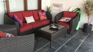 Un ensemble de meubles de jardin en osier avec des coussins rouges, une table basse en verre et une plante en pot.