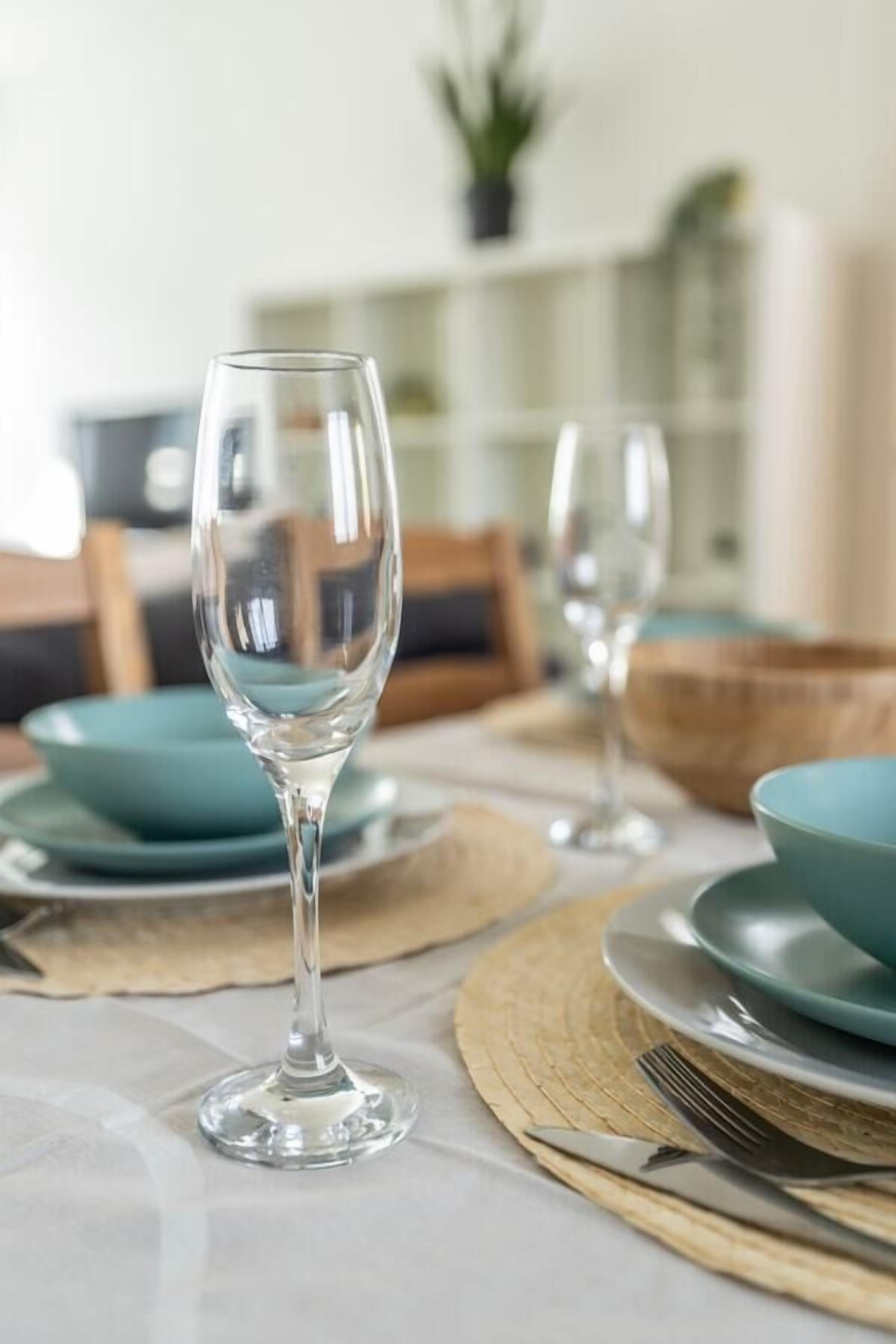 A dining table with clear glassware and teal-colored plates, set with a placemat and a woven placemat.