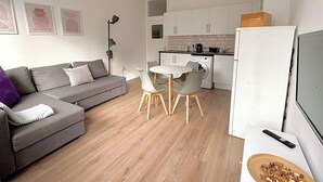 A modern apartment with a grey sofa, a dining table with chairs, a washing machine, and a TV. - Shoreditch Apartments by PrimeCityHosts F6 (Greater London)