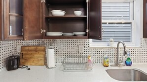 Een keuken met houten kastjes, een betegelde achterwand, een spoelbak en diverse keukengerei.
