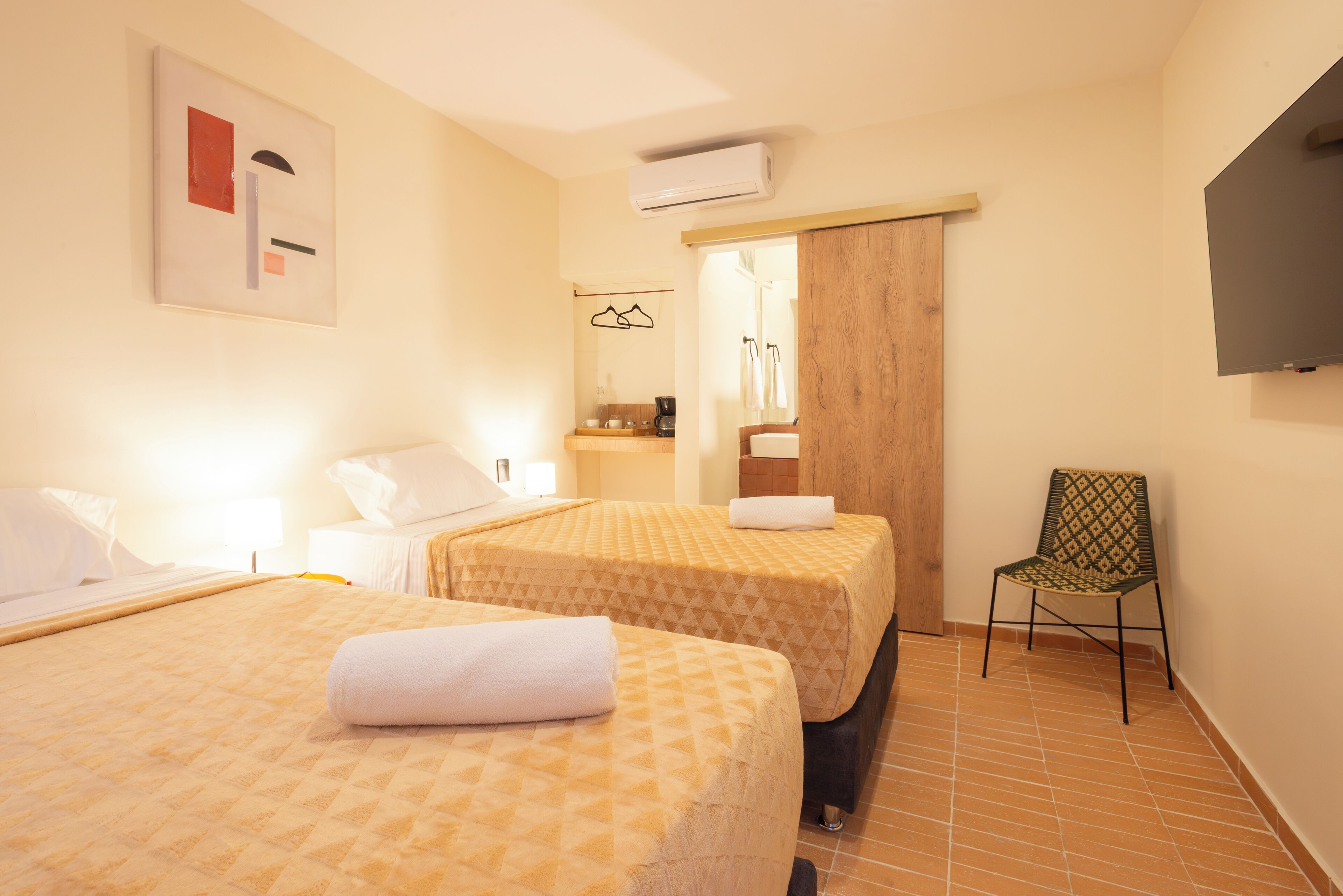 A hotel room with two beds, a chair, a TV, and a bathroom visible through a door.