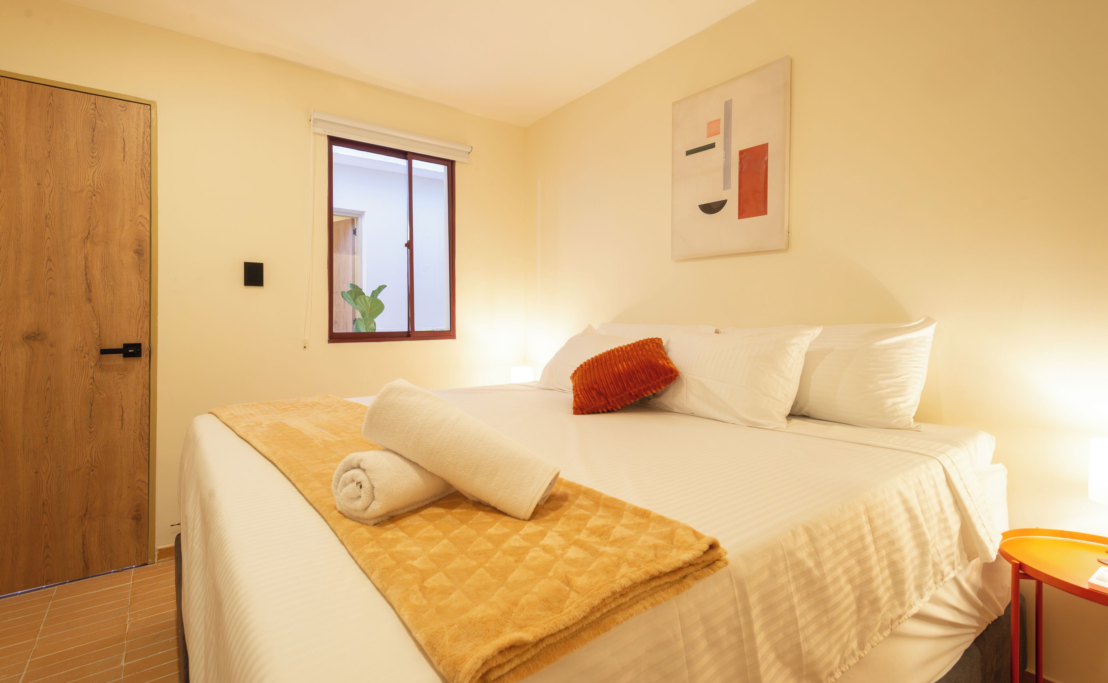 A bedroom with a bed, a window, a door, and a painting on the wall.