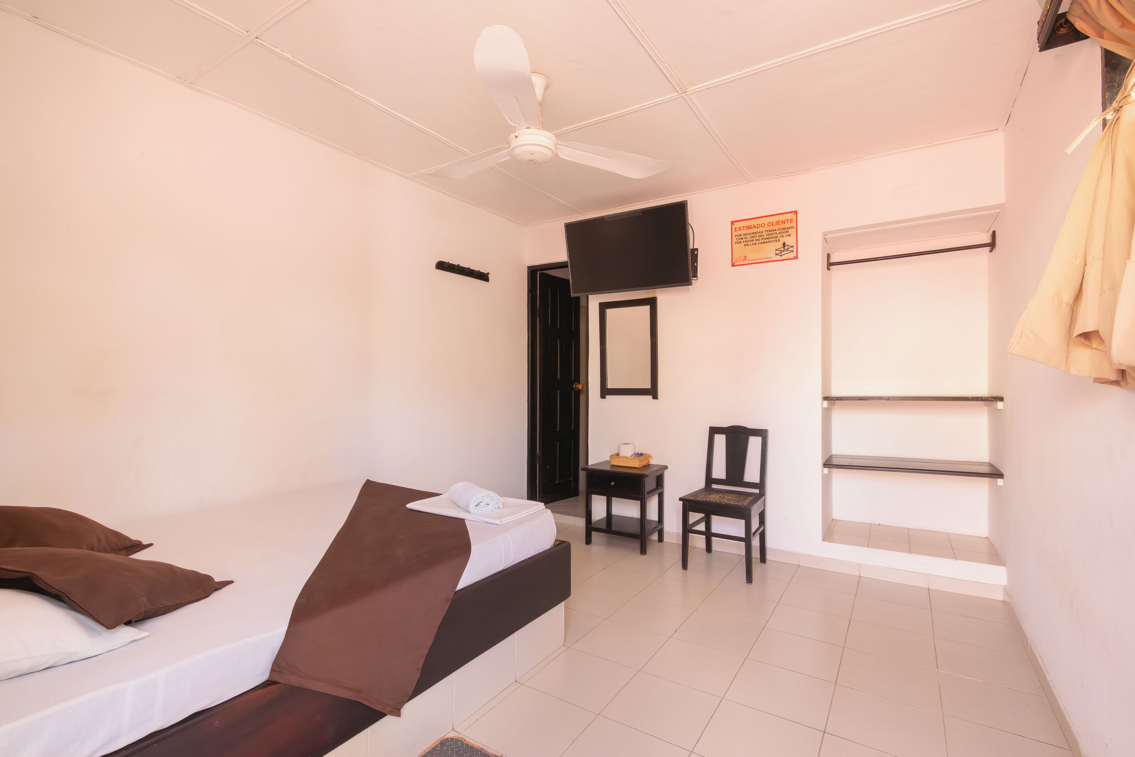 A hotel room with a bed, a chair, a television, and a window.