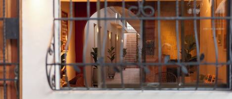A view through a window with metal bars, revealing an interior space with a brick wall, potted plants, and a staircase.