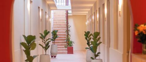 A corridor with potted plants, a tiled floor, and a red archway.