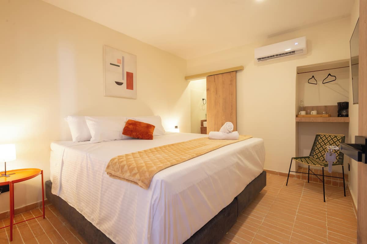 A hotel room with a large bed, a small table, a chair, and an air conditioning unit on the wall.
