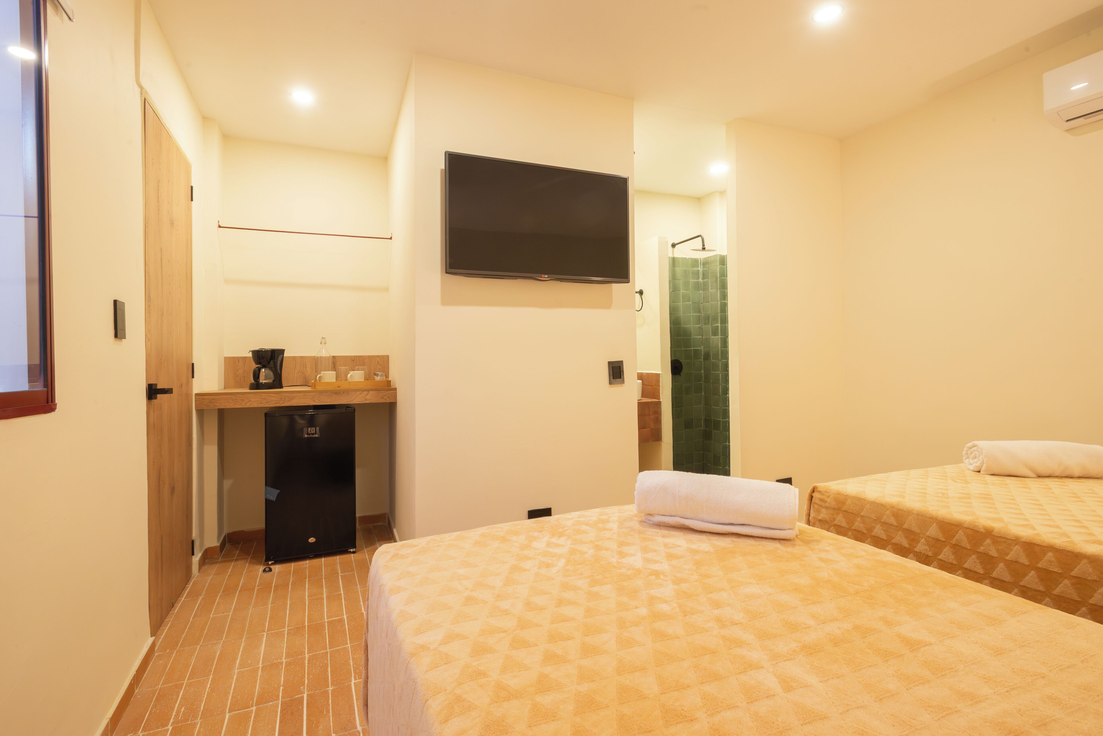 A hotel room with a bed, a small desk with a coffee maker, a TV mounted on the wall, and a shower area.