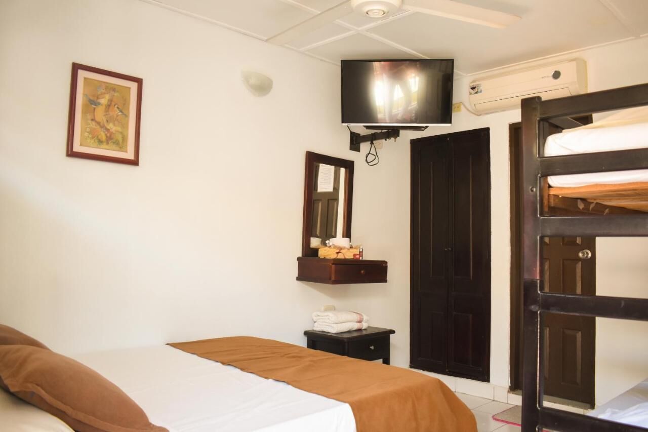 A hotel room with a bunk bed, a flat bed, a television mounted on the wall, a mirror, and a framed picture.
