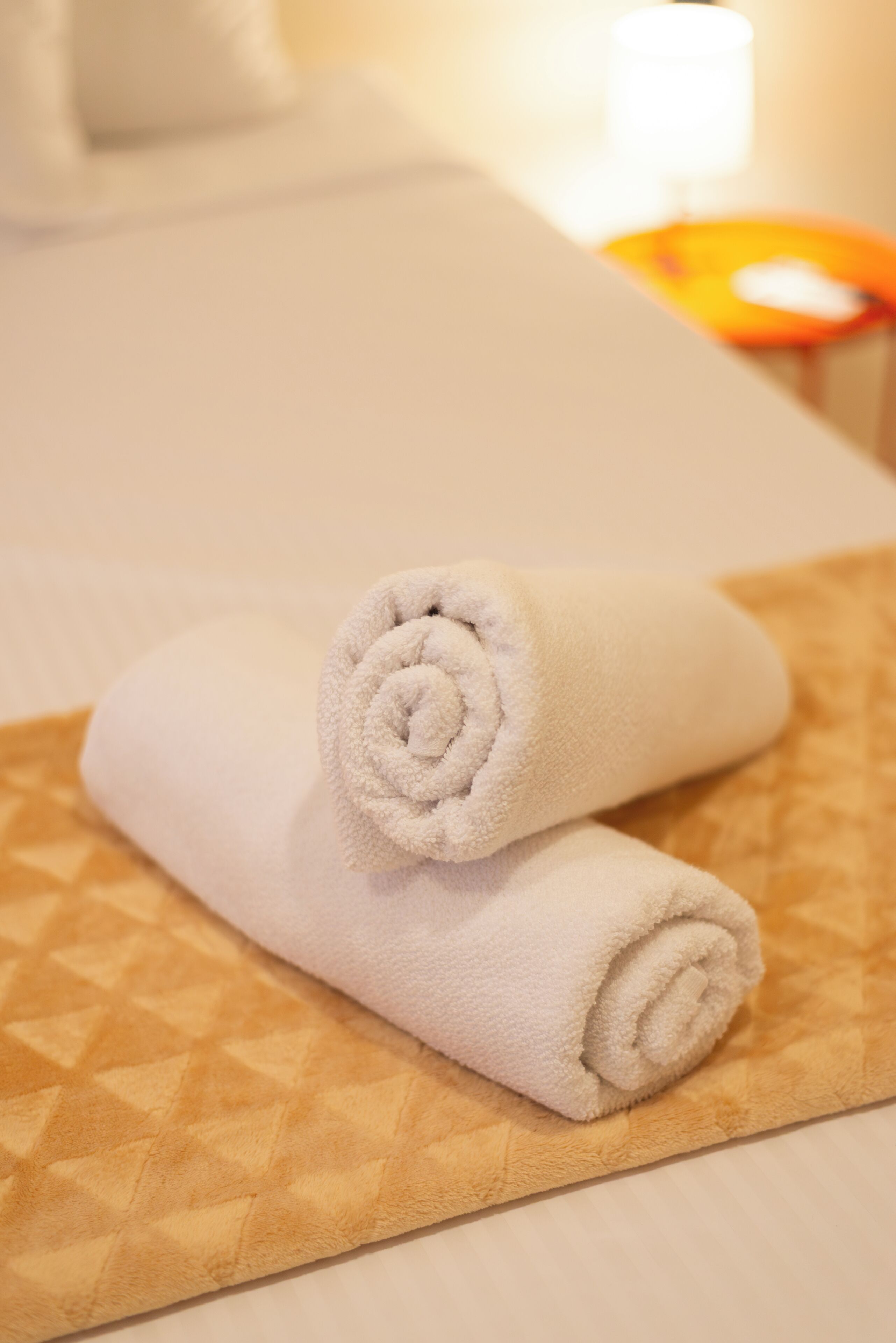 Une serviette blanche, soigneusement pliée, est posée sur un tapis beige à motifs, probablement dans une chambre d’hôtel.