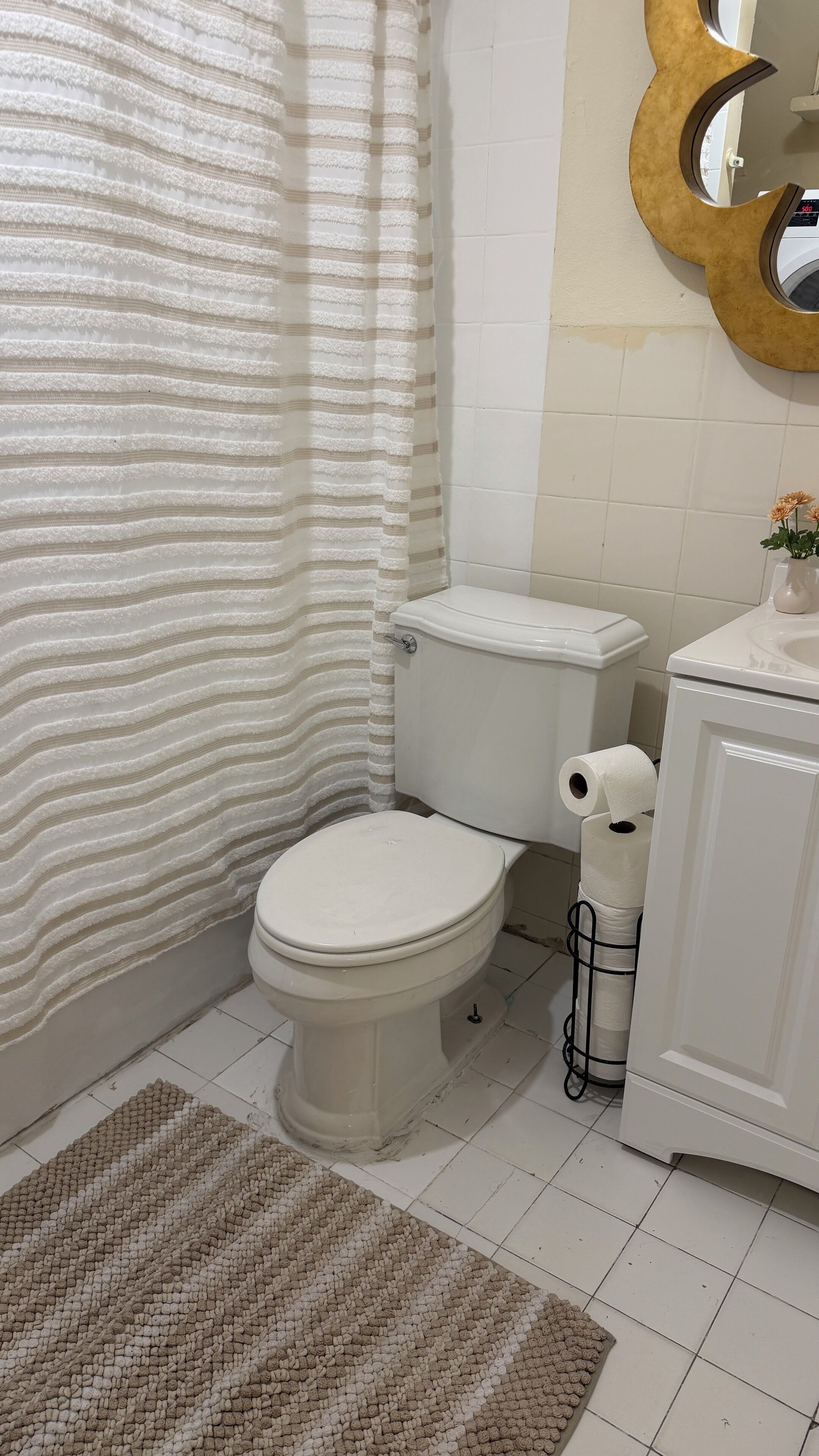 A bathroom with a toilet, a shower curtain, a sink, and a mirror.