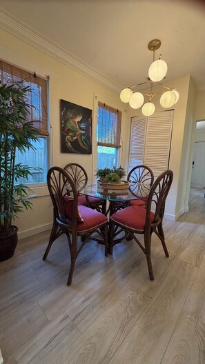 Un coin repas avec une table en verre entourée de chaises en bois dotées de coussins rouges, un luminaire au plafond et un tableau accroché au mur.