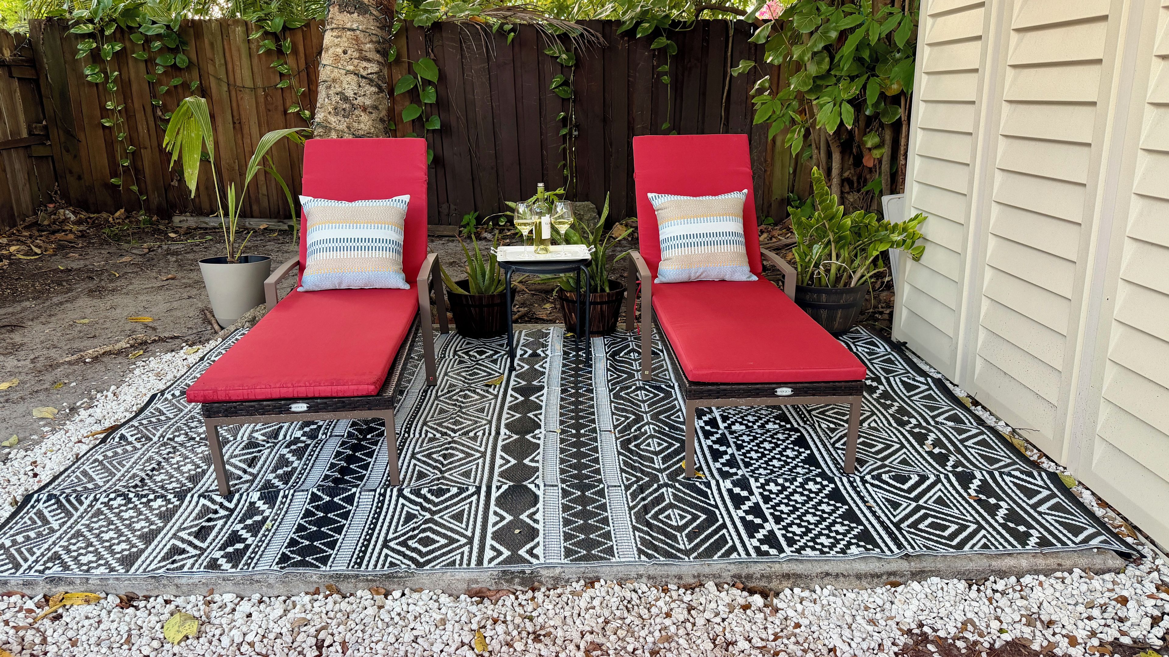 Deux fauteuils rouges confortables avec des coussins à motifs, une petite table sur laquelle se trouvent une bouteille et un verre, et une plante décorative.