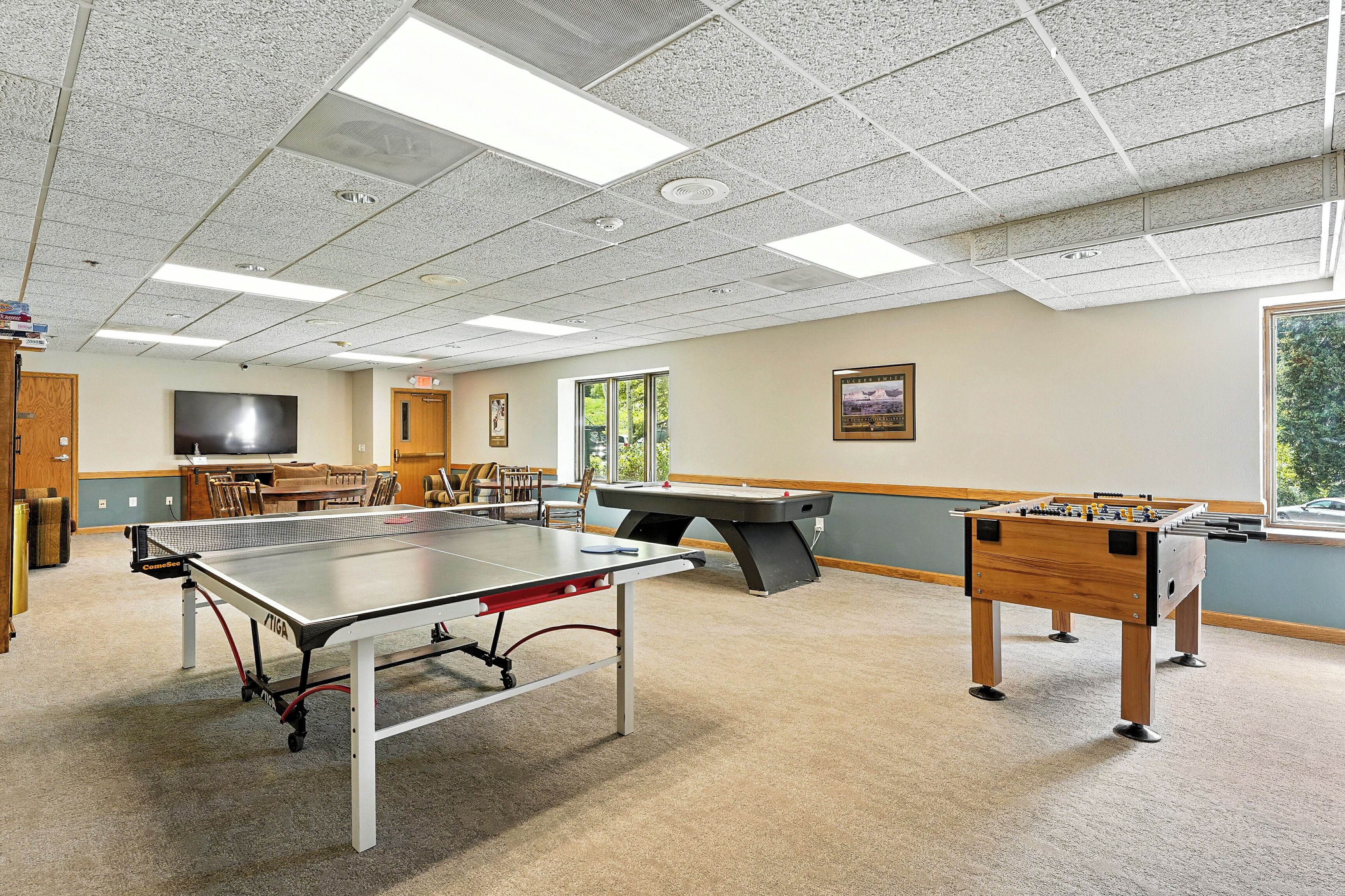 A recreational room with a foosball table, ping pong table, and a pool table.