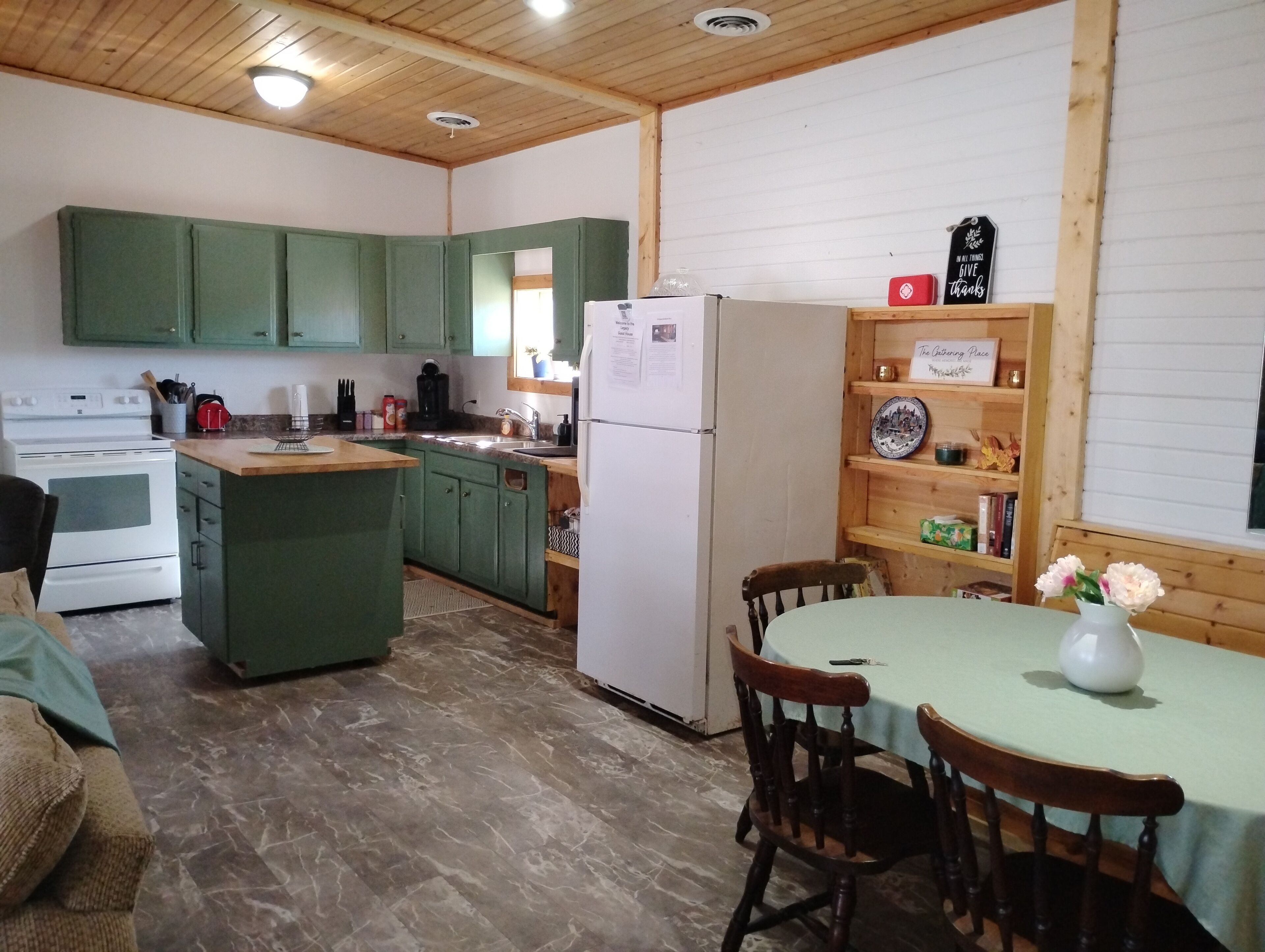 Una cucina compatta con mobili verdi, un frigorifero bianco e un'area pranzo con tavolo e sedie.