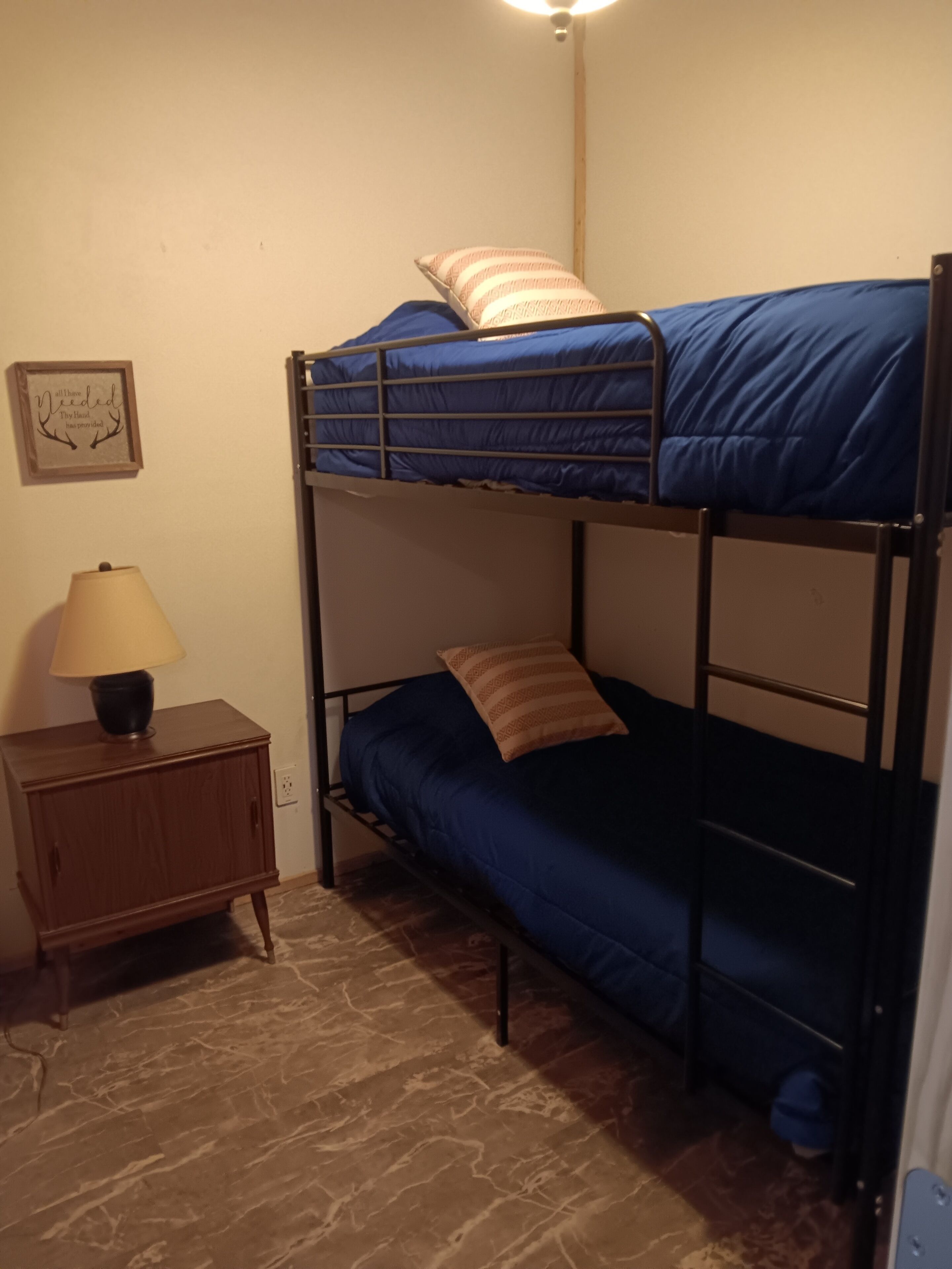 A bunk bed room with a nightstand, lamp, and a framed picture on the wall.