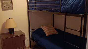 A bunk bed room with a nightstand, lamp, and a framed picture on the wall.