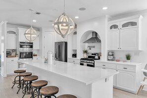 A modern kitchen with white cabinetry, stainless steel appliances, and a central island with bar stools. - Island Escape 3 blocks from beach W/ Heated Pool (Sarasota)