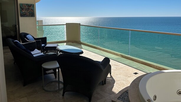 A balcony with a view of the sea, furnished with wicker chairs and a small table, and a bathtub. - Tessoro 802 Oceanfront Luxury Condo (Las Conchas)