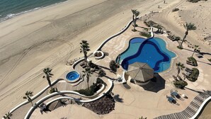 An aerial view of a resort with a large pool, palm trees, and a beach. - Tessoro 802 Oceanfront Luxury Condo (Las Conchas)
