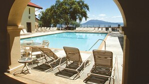 Zona de piscina con sillones reclinables y una mesa, enmarcada por un arco, con vista a la piscina y una montaña.