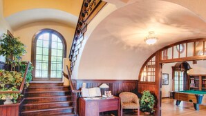 Una habitación amplia con una escalera de madera, una mesa de billar y una zona de estar acogedora con una lámpara y libros.