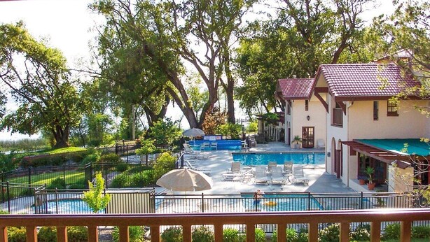 Zona de piscina con dos piscinas separadas, rodeada por una valla, y un edificio con tejado rojo al fondo.