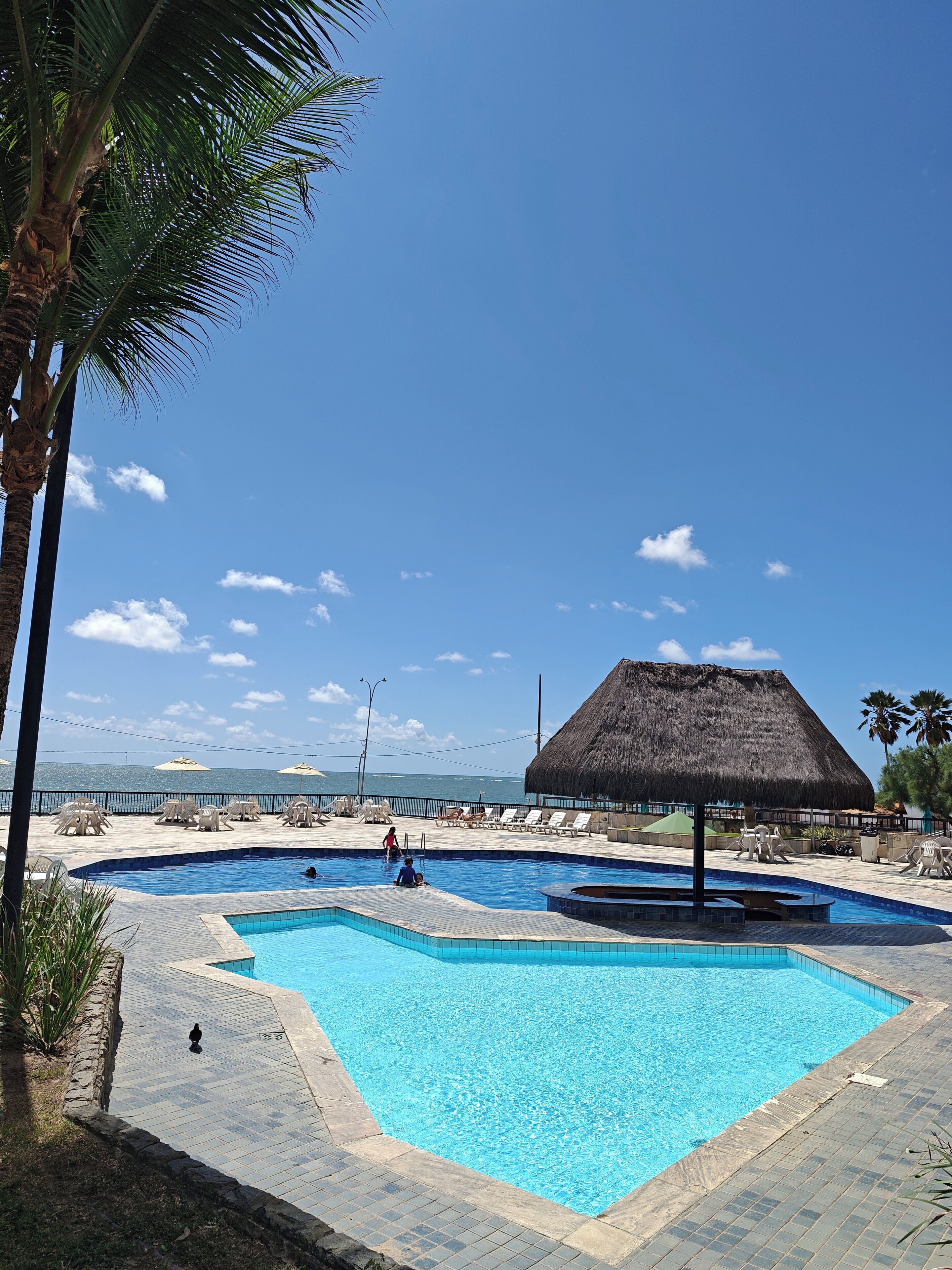 A swimming pool area with multiple pools, lounge chairs, and umbrellas.