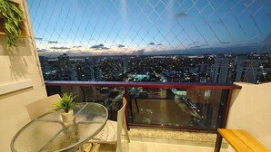 A balcony with a glass table and bench, overlooking a cityscape at dusk. - Premium Flat Golden Beach Beachfront Piedade (Jaboatão dos Guararapes)