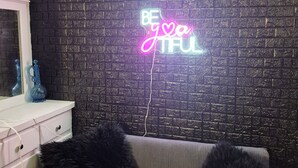 A room with a textured black wall, a neon sign reading "BE YOUR TRUE SELF", a white dresser, and a grey sofa with black cushions. - Stylish Downtown LB Flat – Walk to Everything! (Long Beach)