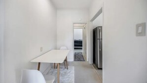 A narrow hallway with a white table and chairs, leading to a kitchen area with a refrigerator. - Stylish Downtown LB Flat – Walk to Everything! (Long Beach)