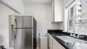 A modern kitchen with a stainless steel refrigerator, a sink, and a window. - Stylish Downtown LB Flat – Walk to Everything! (Long Beach)