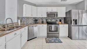 A modern kitchen with white cabinets, stainless steel appliances, and a tiled backsplash. - Modern Texas Home. Prime Frisco Location (Frisco)