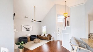 A spacious living room with a high ceiling, a ceiling fan, a large window, and a staircase leading to an upper level. - Modern Texas Home. Prime Frisco Location (Frisco)