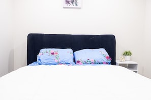 Una cama con ropa de cama estampada, un cabecero oscuro y una mesita de noche pequeña con un reloj y una planta.