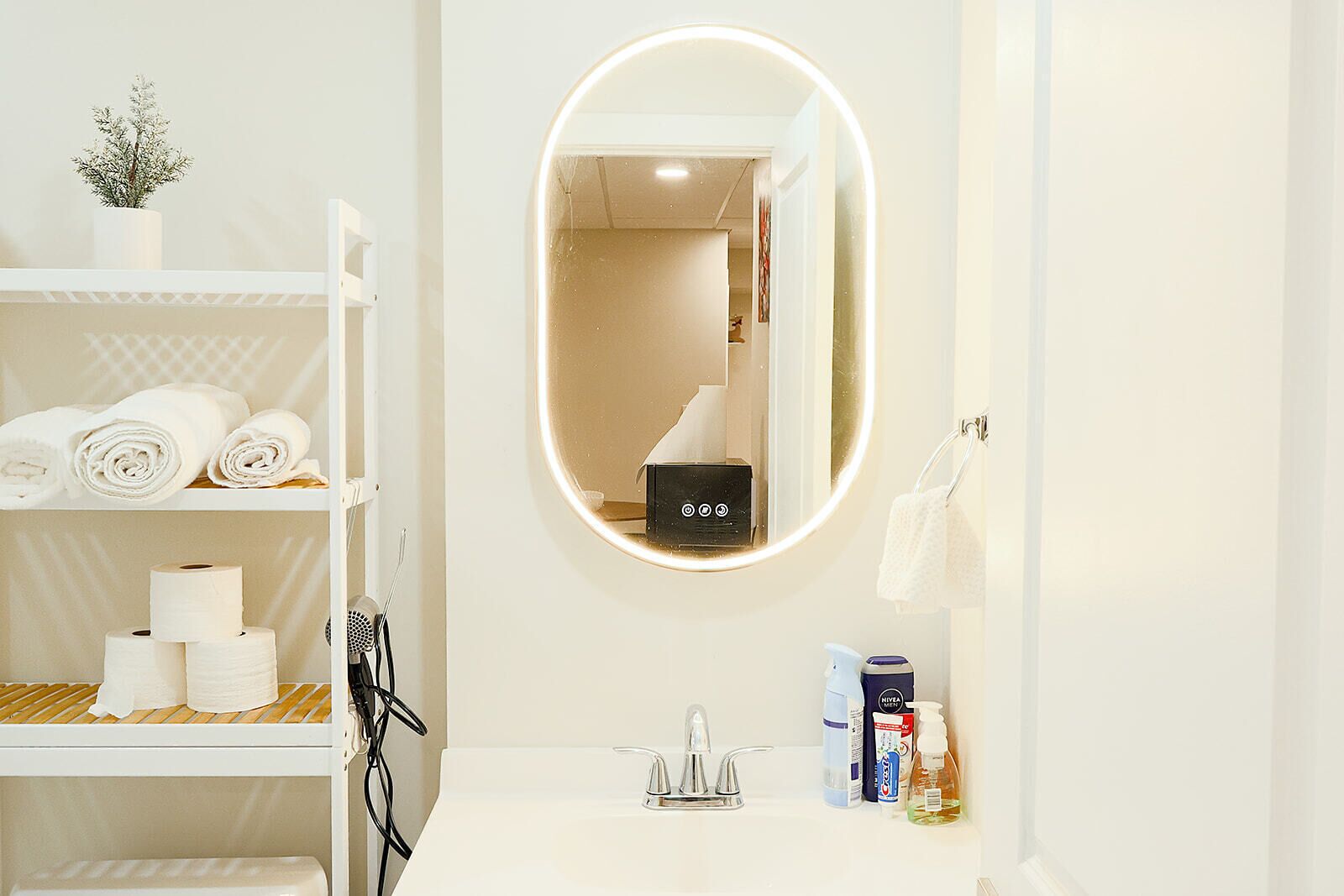 Un baño con espejo, repisas con toallas, papel higiénico, lavamanos y artículos de tocador.