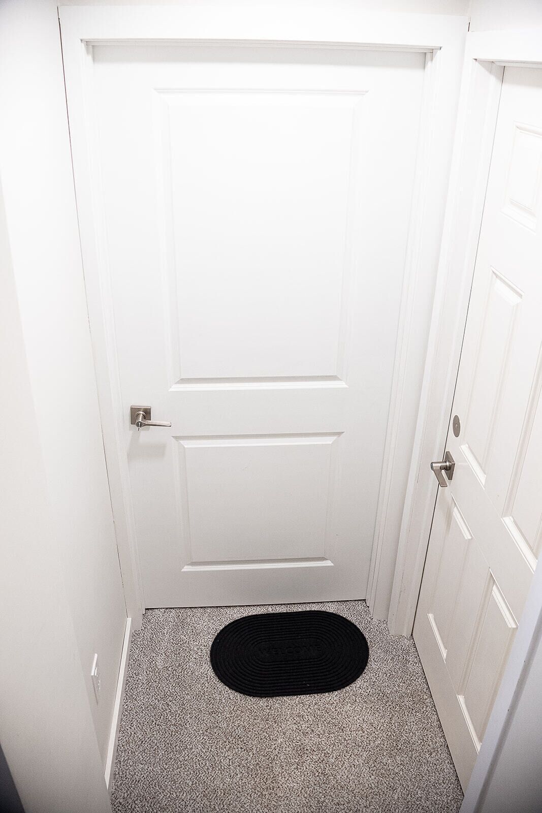 A white door with a doorknob and a black doormat with 'WELCOME' text.