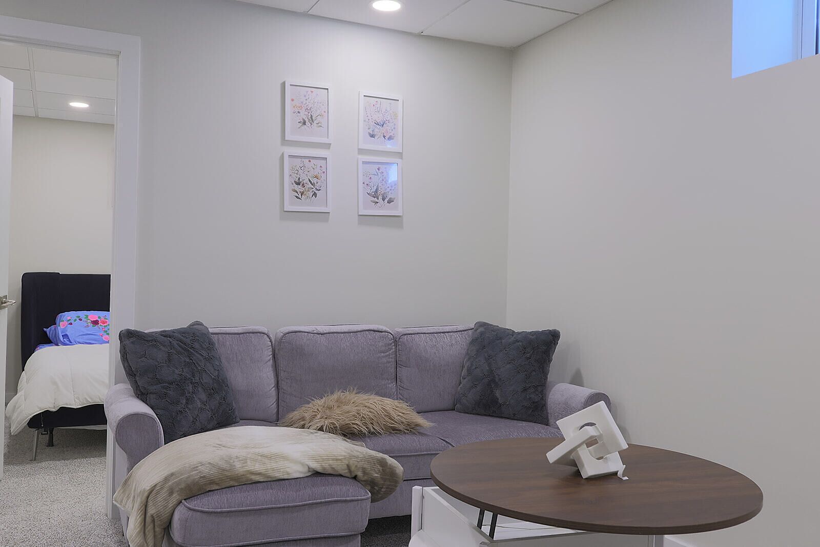Una habitación con un sofá gris, una mesa redonda y tres cuadros florales en la pared.