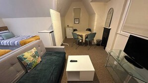 Un espacio habitable compacto con sofá, una mesita, televisor y comedor con sillas.
