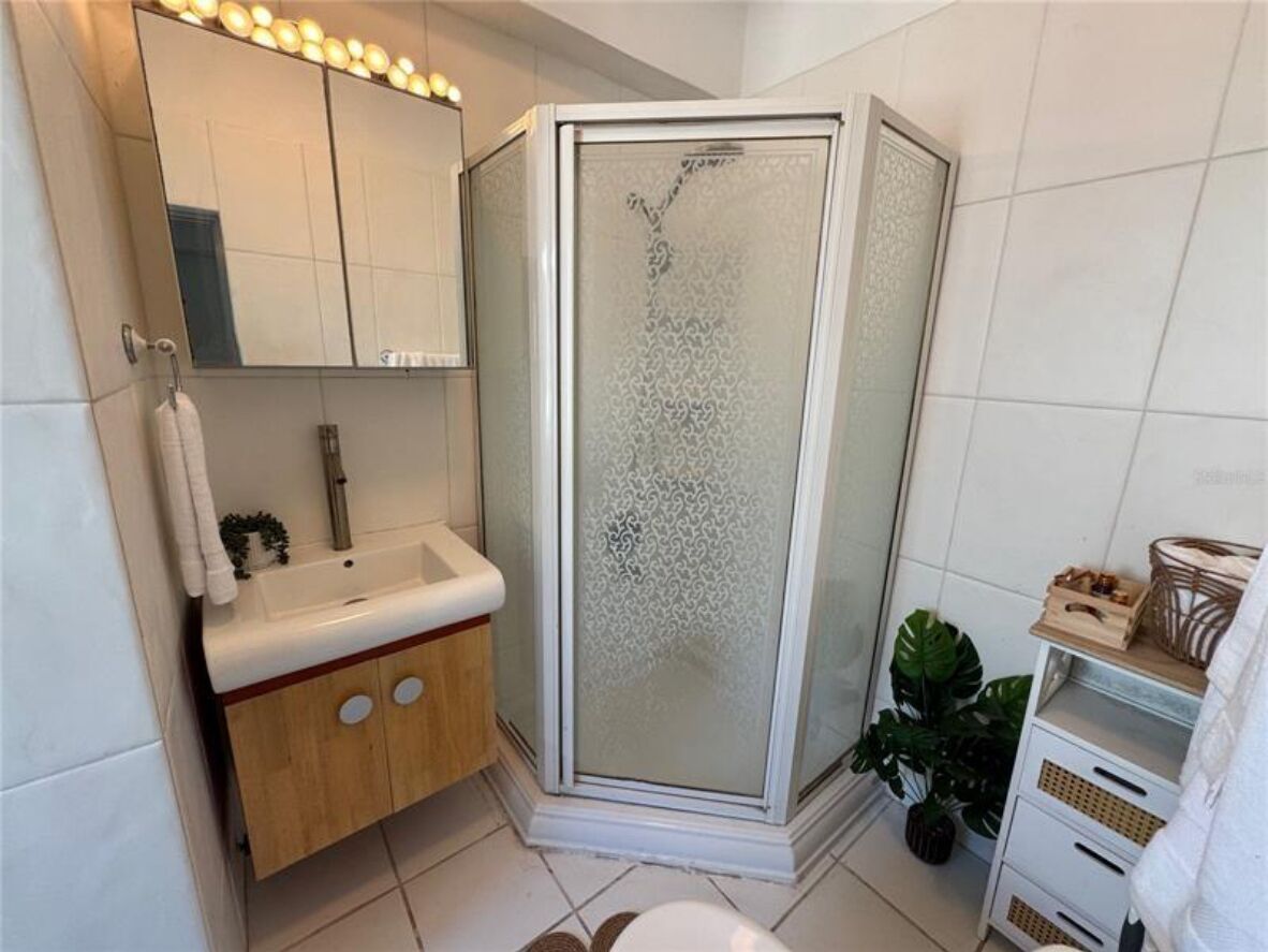 Ett modernt badrum med en dusch som är avskärmad med glasväggar, ett handfat med ett träskåp under och en spegel med belysning ovanför.